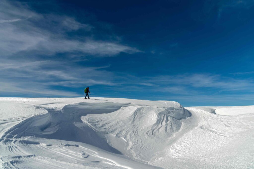Sommet de la Montagnette (1972m), randonneuse marchant en direction du sommet sur de la neige travaillée par le vent