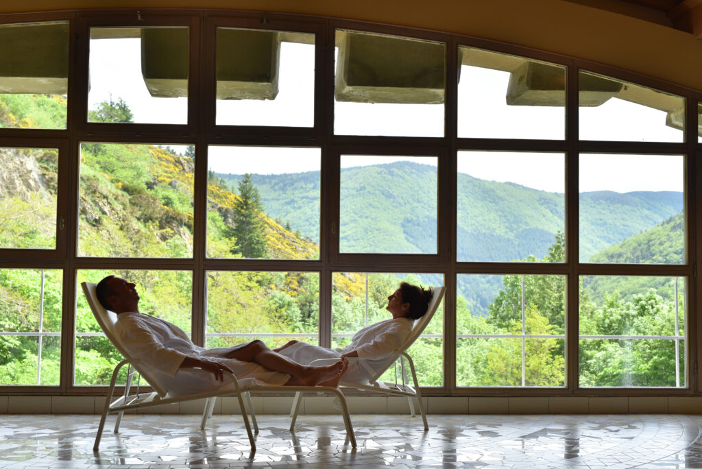 Deux personnes allongées sur des chaises longues profitant de l'espace spa des thermes de Saint Laurent-les-Bains face aux montagnes