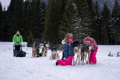 Deux enfants au premier plan - avec des chiens de traineau, un parent derrière. Dans le neige